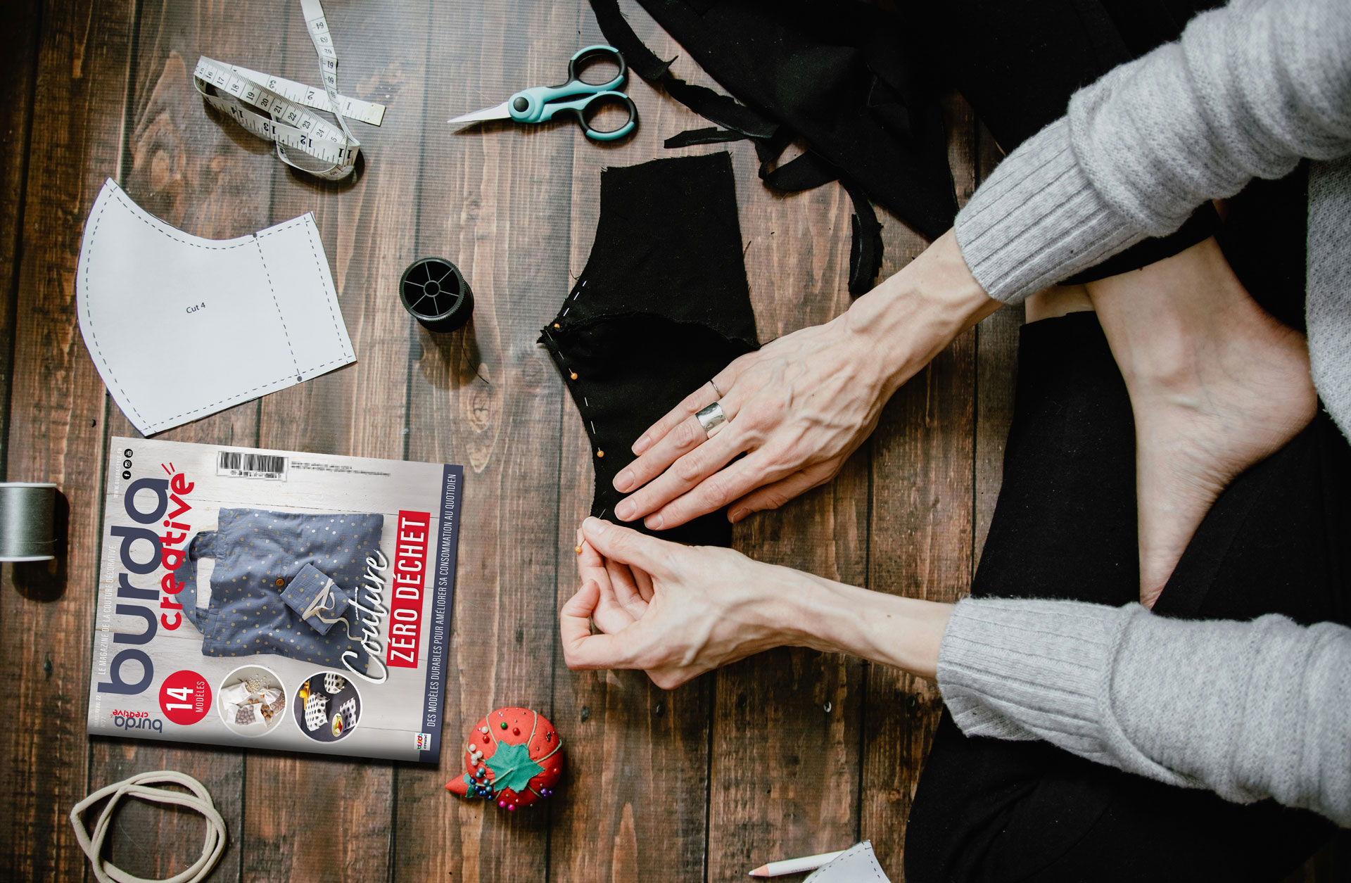 Scène d'atelier de couture avec mains de femme en train de coudre, avec le magazine Burda Creative en évidence, illustrant l'application du logo pour un magazine de couture dans un contexte créatif.
