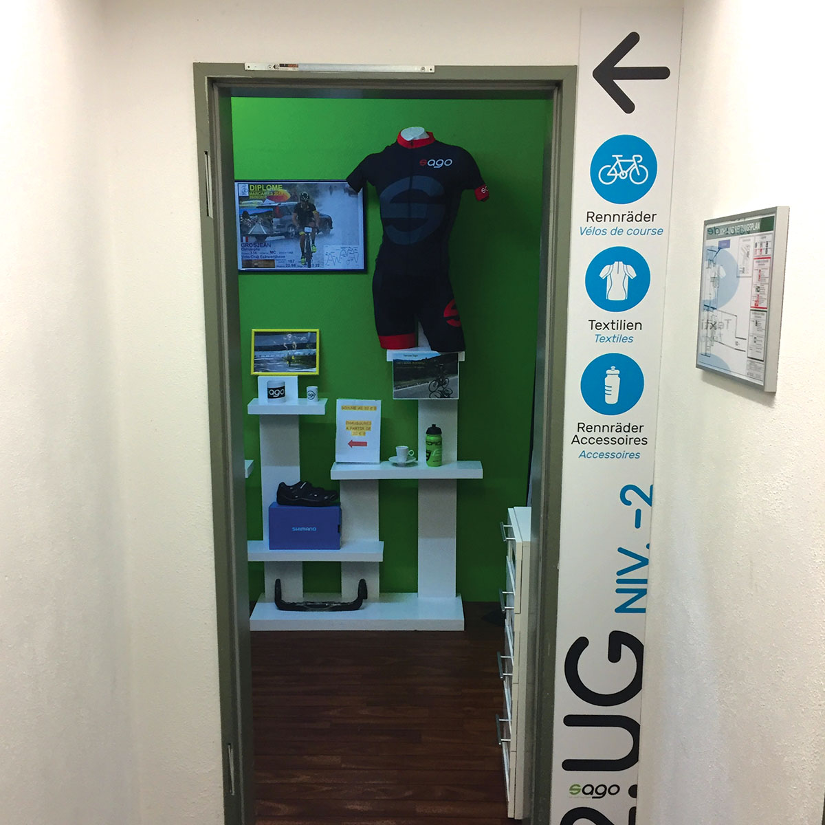 Panneau de signalétique murale dans un magasin de vélos : indication pour le niveau -2 avec pictogrammes de vélos de course, textiles et accessoires.